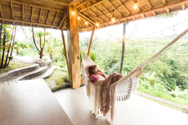 Woman admiring tropical nature and rice paddies from a hammock on vacation in Bali, Indonesia - sustainable architecture
